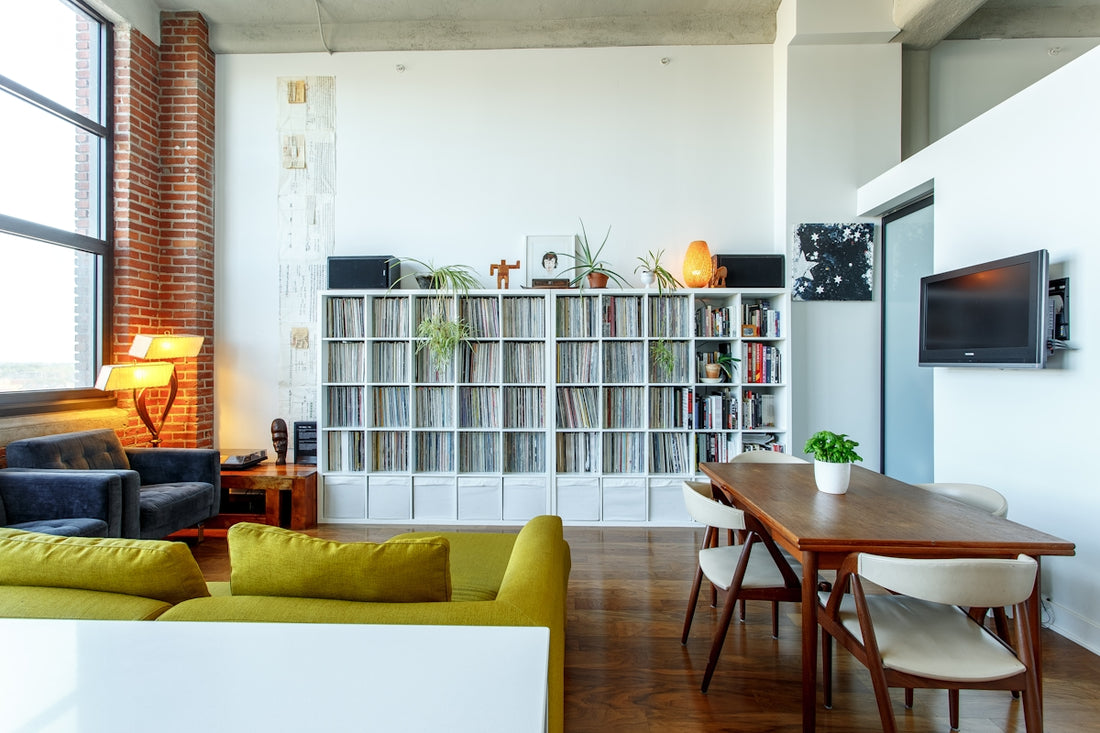 A living room with a large record shelf, green sofa, and wooden dining table
